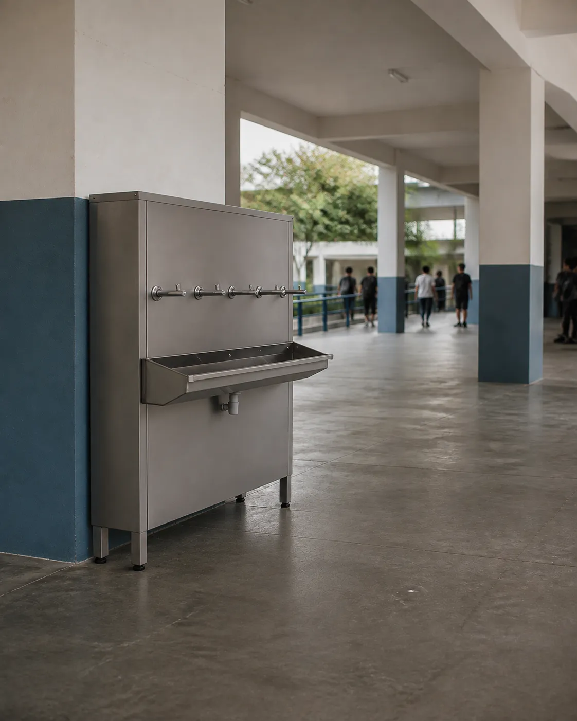 Bebedouro industrial Refriágua em aço inox com seis torneiras e aparador corrido, no corredor coberto de uma escola